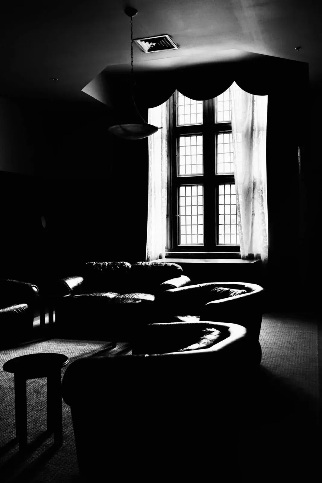 Daylight through a tall window illuminating chairs in a dark room
